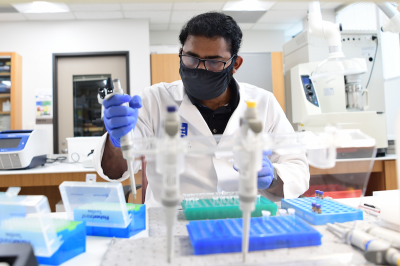 A researcher wearing a face mask works in a lab.