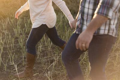 Photo of a couple walking hand in hand through a grassy area only showing couple from the chest down. 