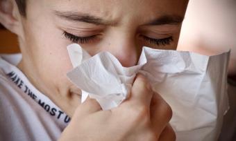 Image of a young boy sneezing into a tissue.