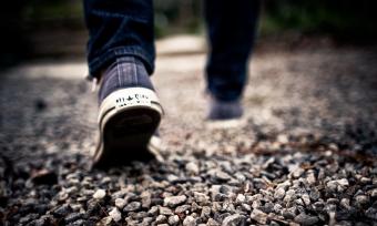 Close up photo of sneaker-clad feet walking away from the camera on gravel. 