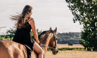 A photo of a woman riding a horse taken from behind.