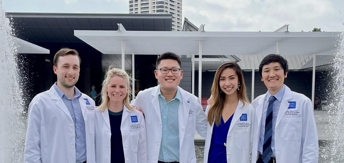 Five people in white coats stand in front of a fountain.