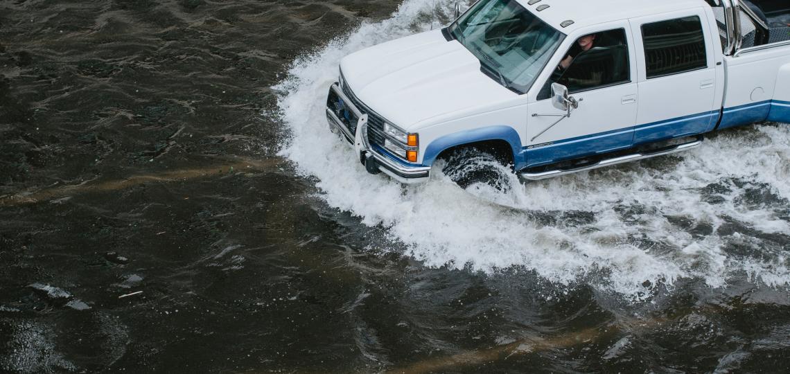 A white truck drives through a flooded roadway. Flood waters can cause a variety of health concerns, including allergies, trauma and the spread of infectious diseases.
