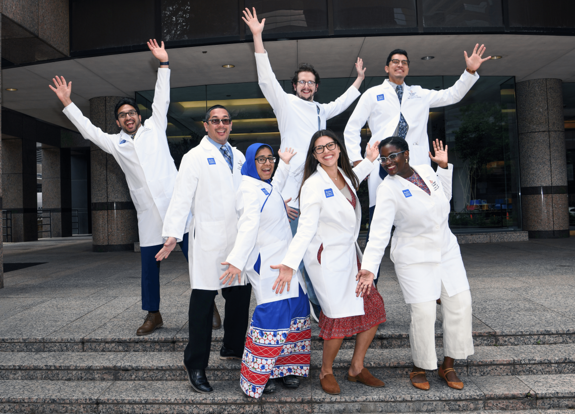 The Pediatric Critical Care Medicine Fellowship Graduating Class of 2022 pose with arms spread wide in a silly pose on the steps of the Debakey Library.