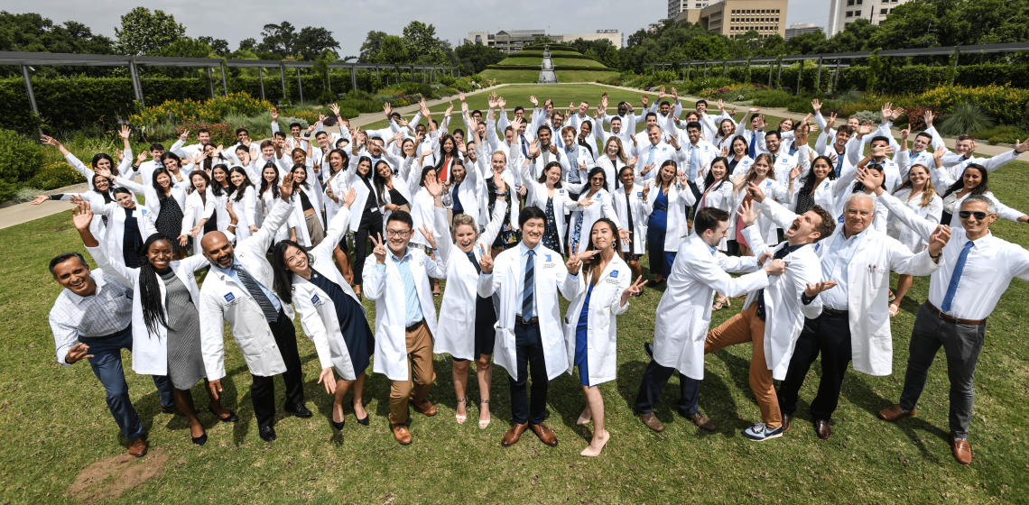 A large group in white coats in a lush garden doing silly poses