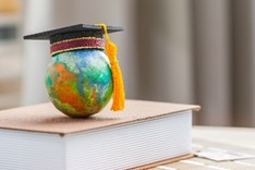 A small globe with a graduation cap sitting on top of a book. 