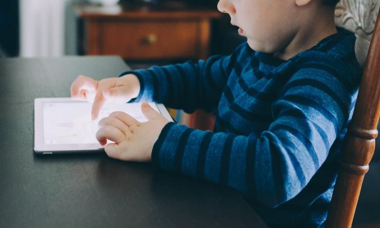 Photo of a child sitting at a table playing on a tablet.