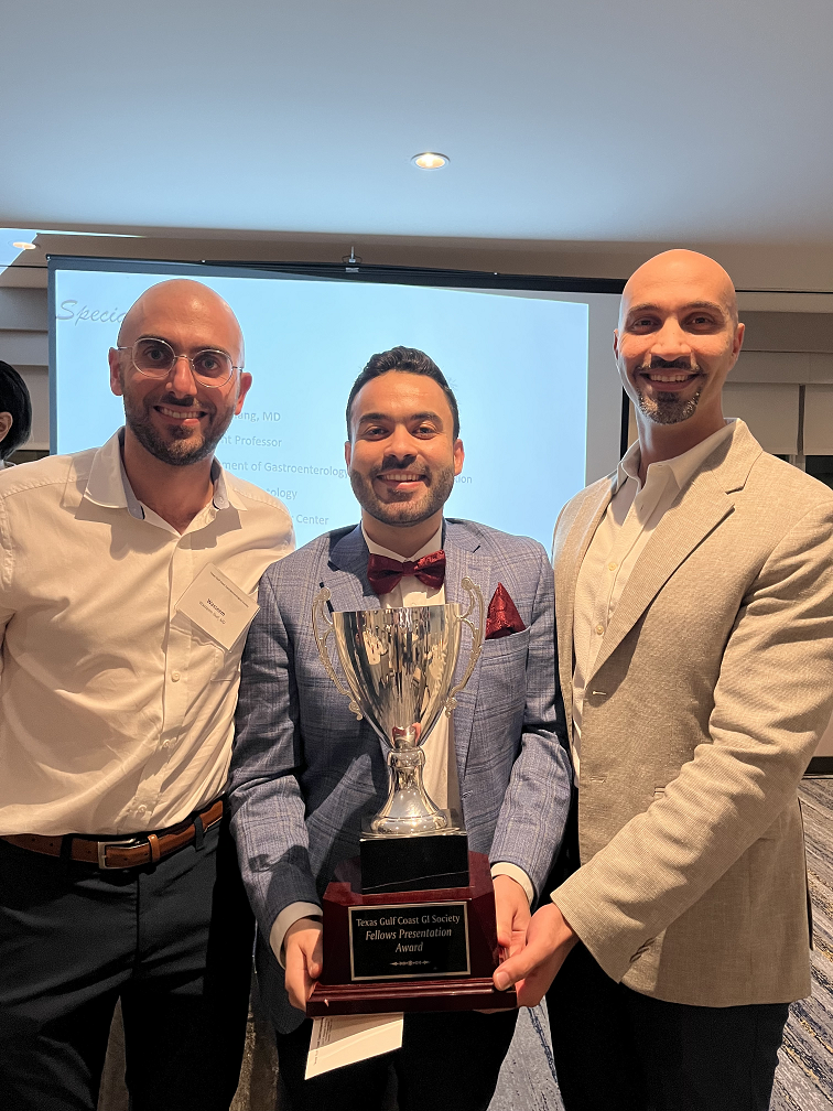 3 people smiling with one in middle holding an award