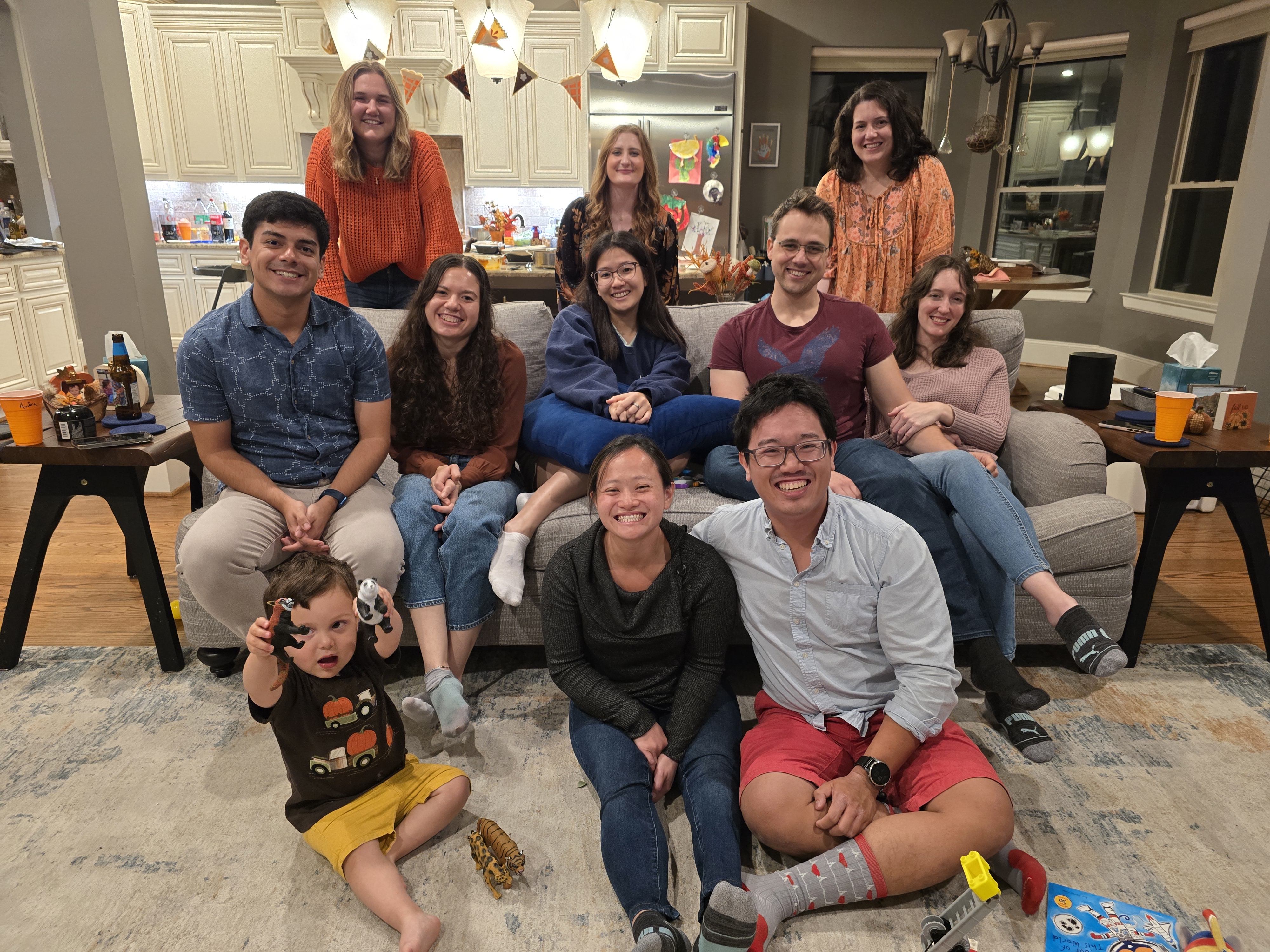 group of eleven people smiling while sitting on the floor and couch in a home