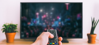 A person pointing a remote control at a television while watching a movie at home.