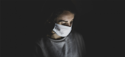 A person wearing a face mask reading information on a laptop.