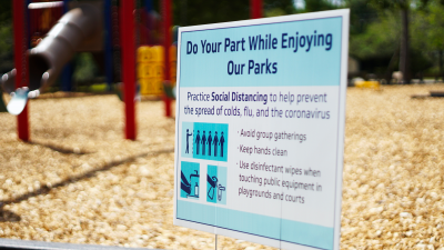 A sign suggesting social distancing posted in front of a playground.