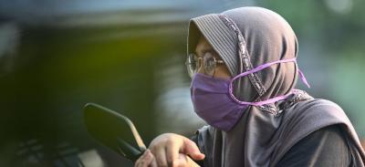 A person wearing a purple protective face mask while sitting on a motorcycle.