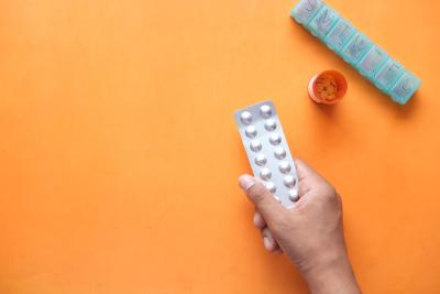 Hand holding white pills on an orange background