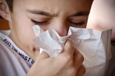 Image of a young boy sneezing into a tissue.