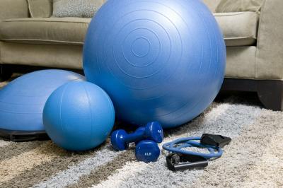 Blue exercise ball, weights and band sitting on the floor in front of a grey couch. 