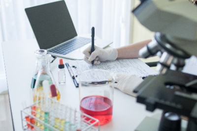 A research working in a lab with microscope and a lab top completing paperwork.