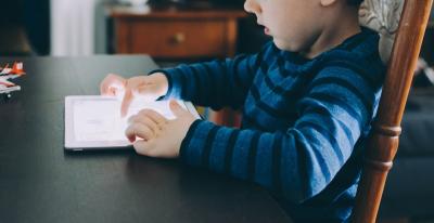 Photo of a child sitting at a table playing on a tablet.