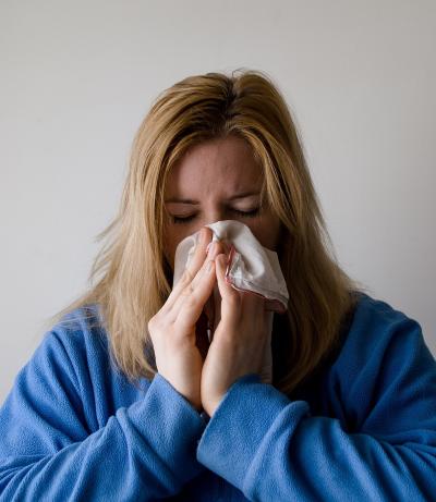 Blonde woman sneezing into a tissue