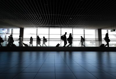 Photo of people in silhouette walking in front of a window at the airport. 