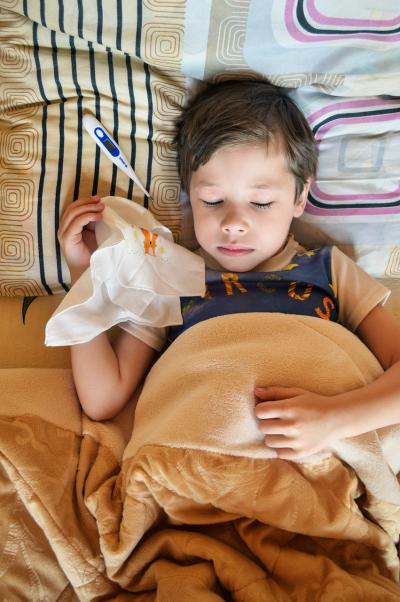 Photo of a little boy in bed with a thermometer and a hankerchief