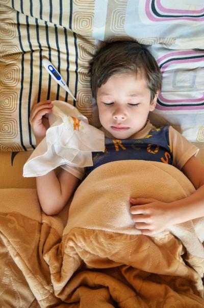 Photo of a little boy in bed with a thermometer and a hankerchief  