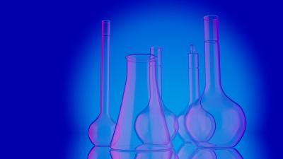 Photo of different sized beakers with blue and pink lighting, represents a general idea of lab work.