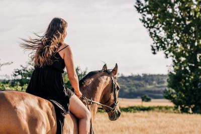 A photo of a woman riding a horse taken from behind.