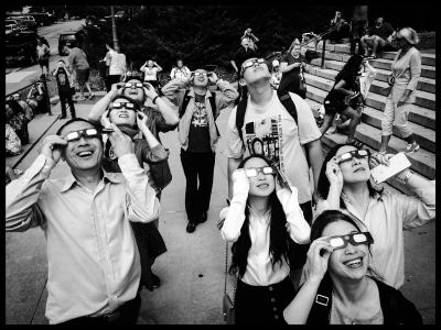 Photo of a group of people wearing solar eclipse glasses looking up at the sky.