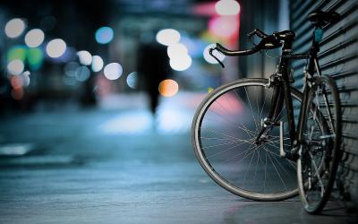 Photo of a bike on a sidewalk, leaning on a garage door, at night with a blurred street background. 