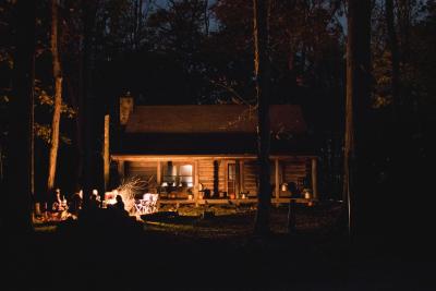Photo taken at night of a group of people sitting around a camp fire in front of a cabin. 