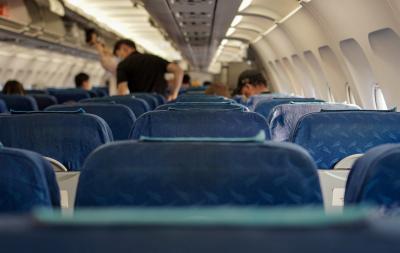 Photo of empty seats on an airplane with travelers blurred in the background. 