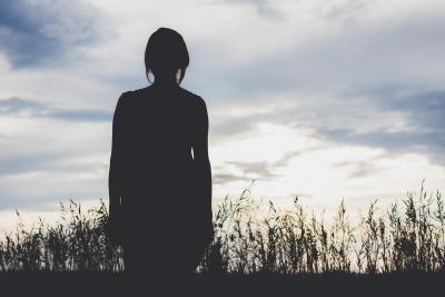 Silhouette of female standing in front of tall grass.