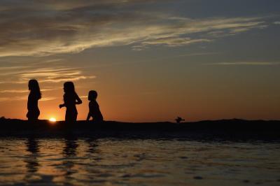 Silhouette of children running on beach at sunset.