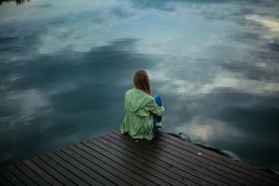 Photo of a woman sitting alone on a dock in the dim fall light. 