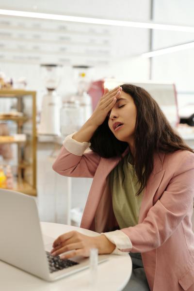 A woman is sitting at work with her hand on her forehead and eyes closed, she is coming down with a cold.