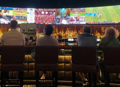 Four people sitting at bar watching sports games on TV