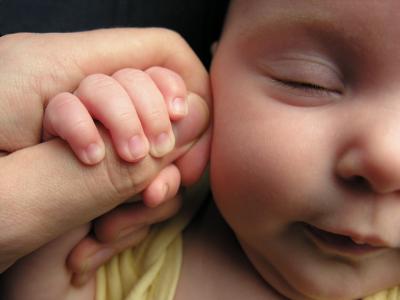 A newborn baby holds on to an adult's thumb.