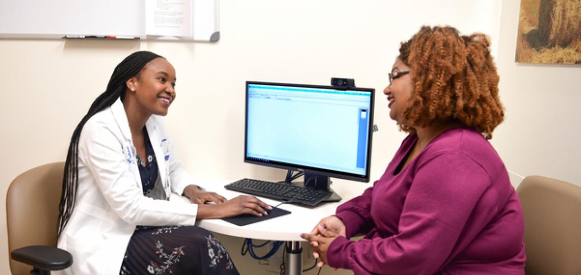 A doctor and her patient are sitting and discussing care and treatment in front of a computer.