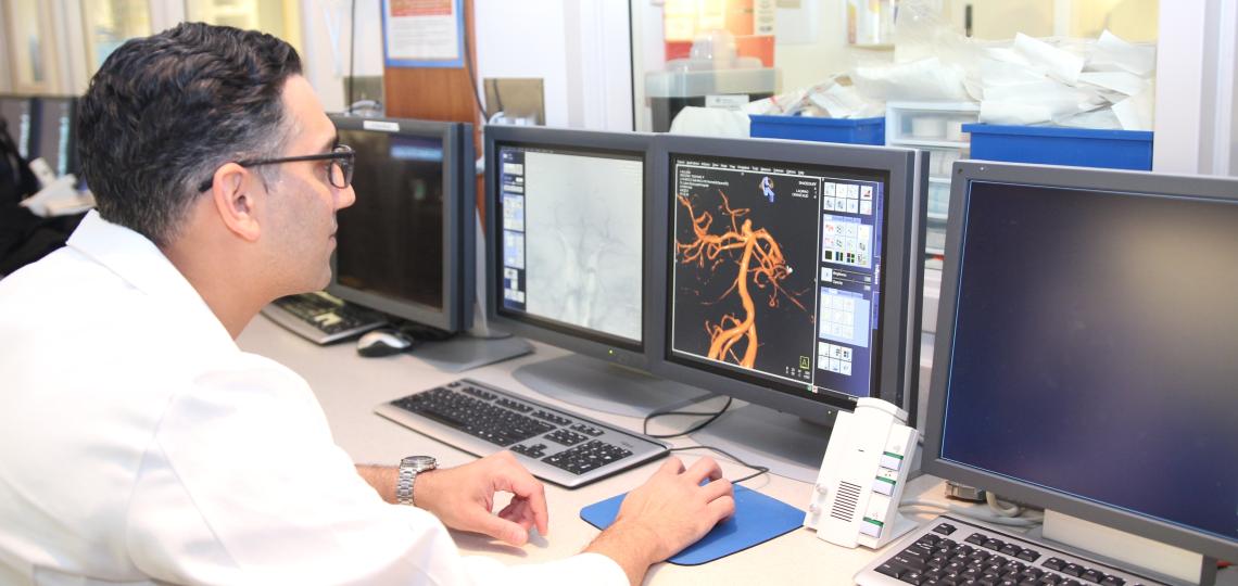 Three doctors studying the scan of a cerebral image on computer screens.