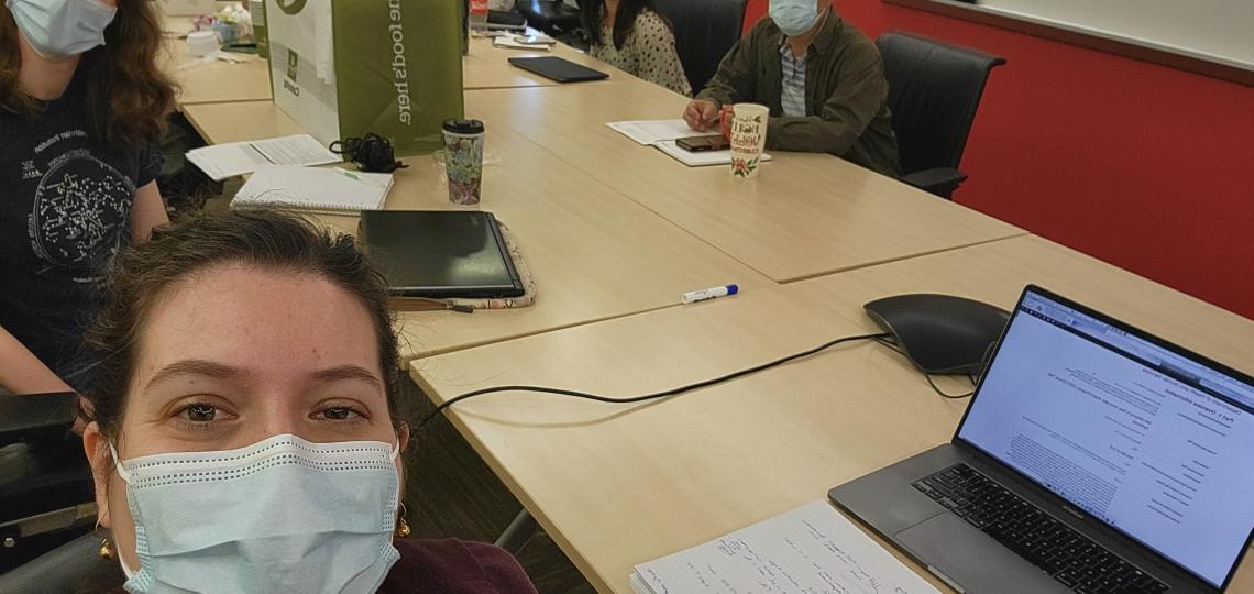 A group of five masked people having a meeting in a conference room.