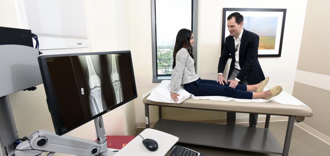 A male doctor examining the knee of a female patient.