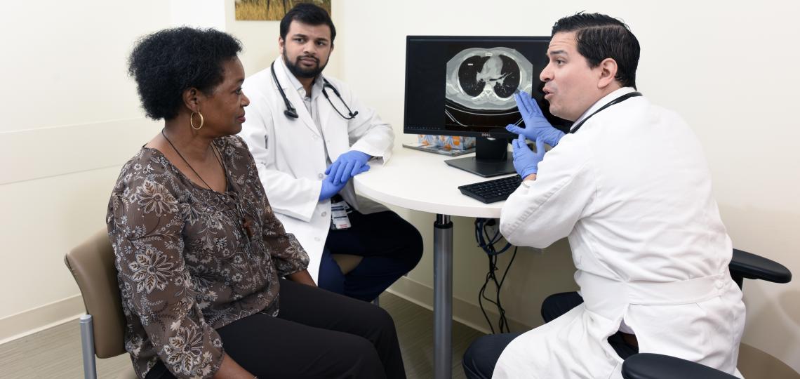 Two male doctors discussing a medical image of the inside of the body with a female patient