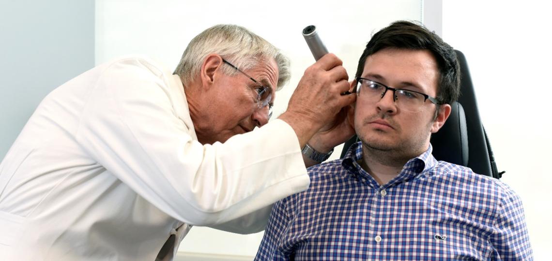 A male physician looking into the ear of a male patient with an otoscope.