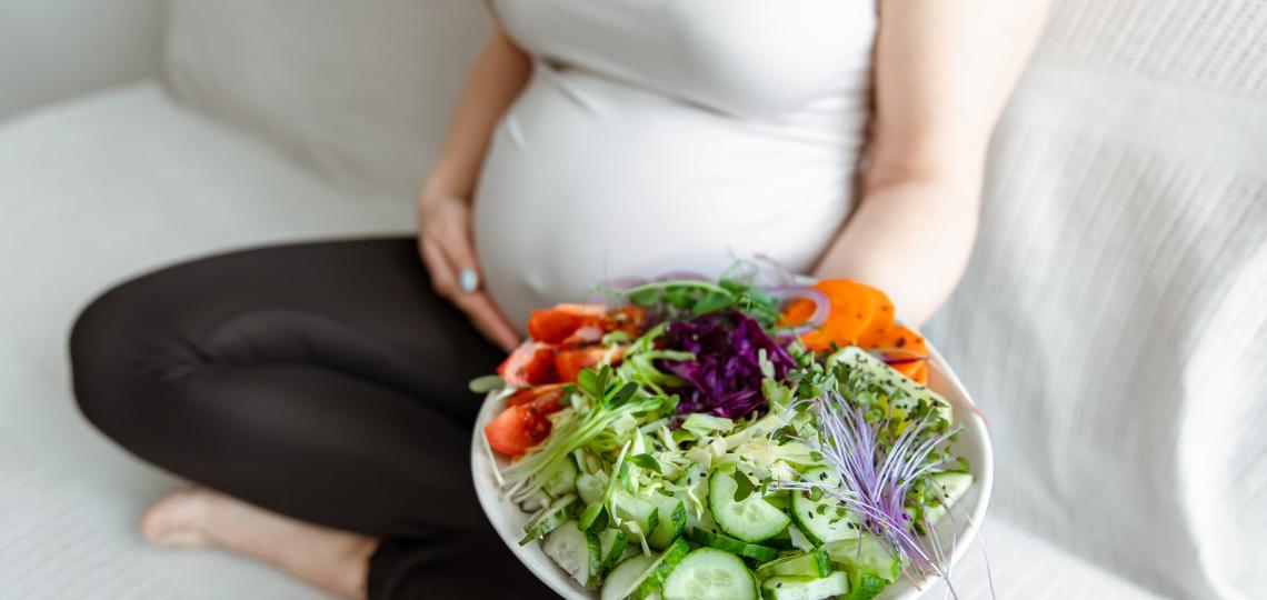 A pregnant woman eating a plate of vegetables.