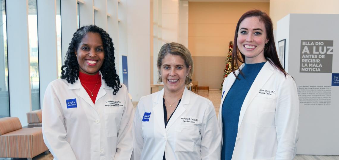 Three female doctors in white lab coats smiling.