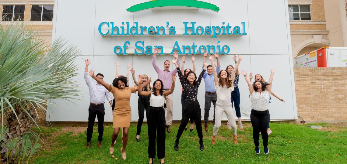 Several residents jumping in front of the Children's Hospital of San Antonio sign