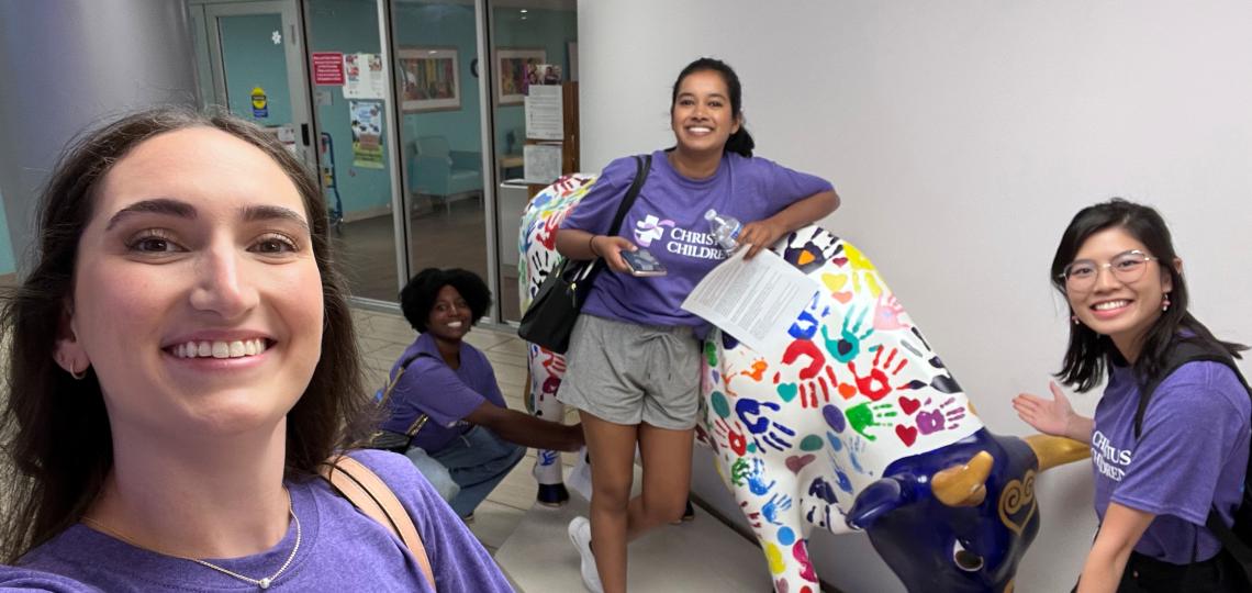 Four interns standing with a color cow statue