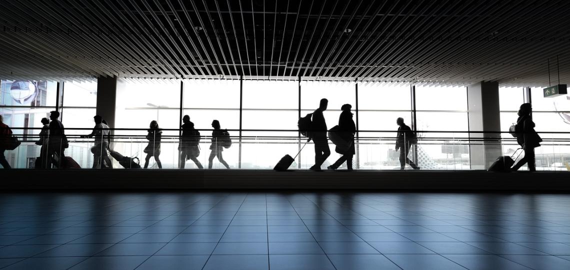 Photo of people in silhouette walking in front of a window at the airport. 