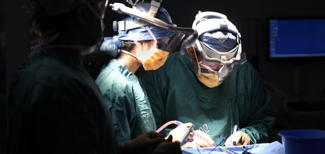 A darkened operating room, with two surgeons using tools on a patient